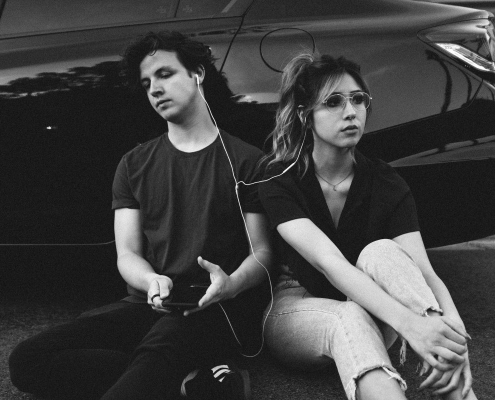 grayscale photo of man and woman leaning on vehicle