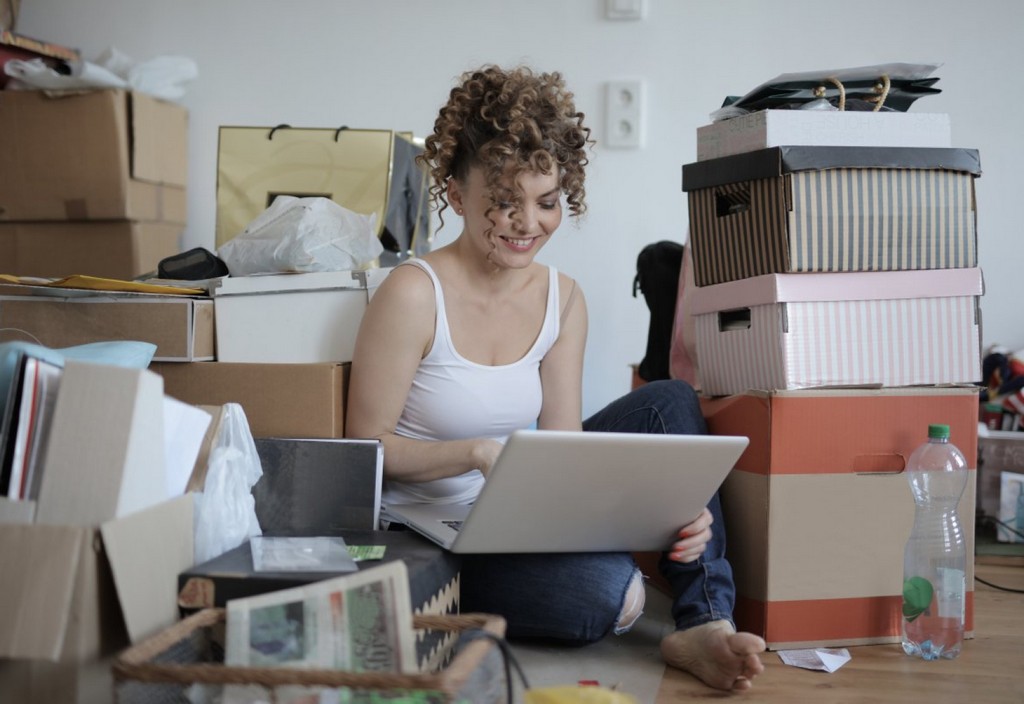 Female shopaholic with laptop shopping online in messy living room