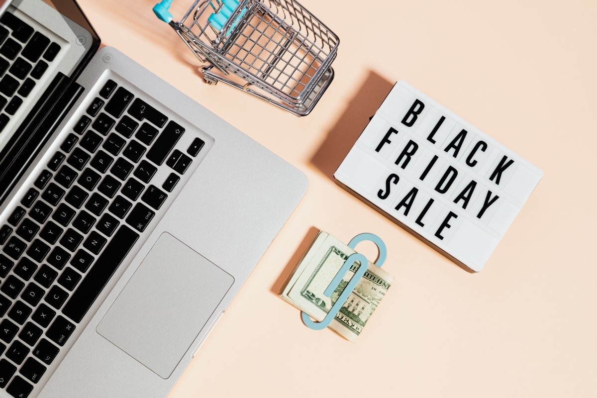 Top view of silver macbook beside a shopping cart and black friday sale signage