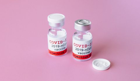 Two covid vials on pink surface