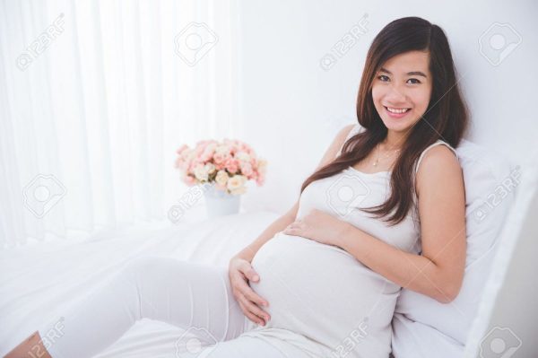 43524735 A Portrait Of A Beautiful Asian Pregnant Woman Leaning On A Bed Smiling