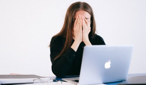 Woman with hands on her face in front of a laptop