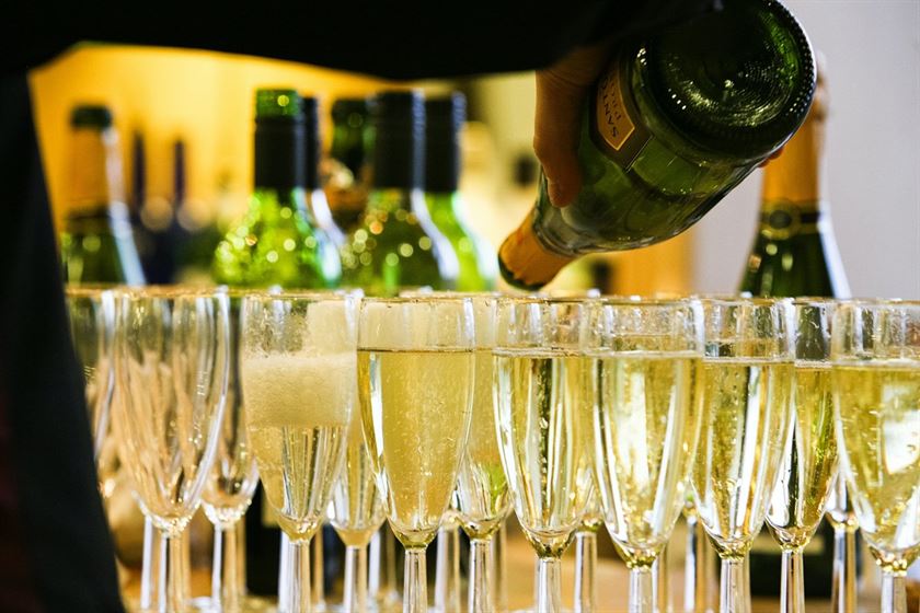 a-waiter-pouring-champagne-into-a-group-of-glasses-with-more-bottles-out-of-focus-in-the-background-stockpack-unsplash.jpg A waiter pouring champagne into a group of glasses, with more bottles out of focus in the background.