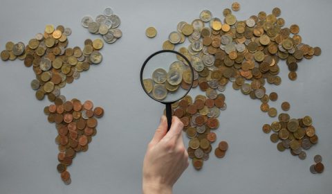 Anonymous person with magnifying glass over world map of coins