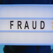 A person with handcuffs holding a sign that says fraud