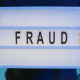 A person with handcuffs holding a sign that says fraud