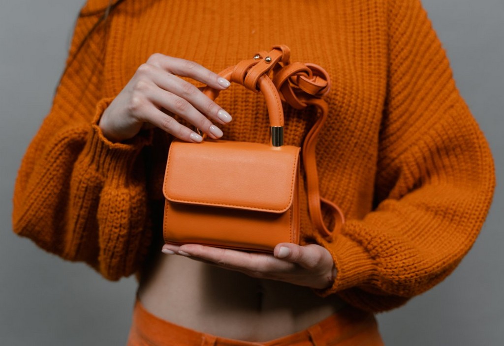 Mini orange leather bag held by a person wearing knitted sweater