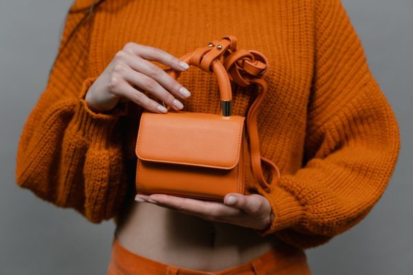 Mini orange leather bag held by a person wearing knitted sweater