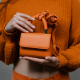 Mini orange leather bag held by a person wearing knitted sweater