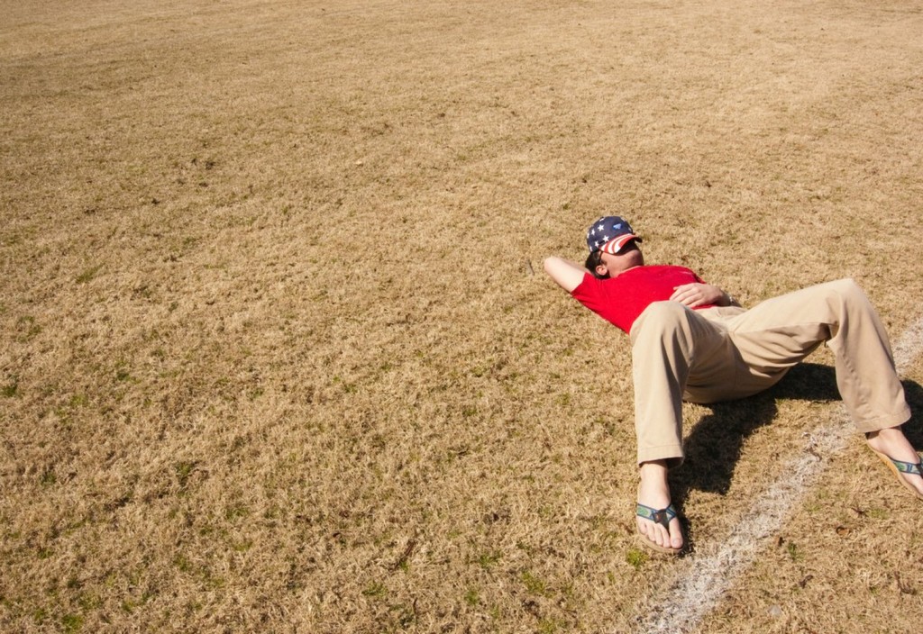 man in red top lying on lawn field during daytime