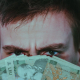 Serious young male covering face with banknotes