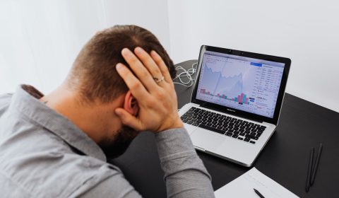 Man with laptop on desk terrified by stock market chart