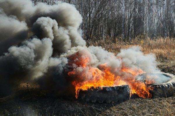 Burning rubber car wheels with thick black-gray acrid smoke. A barrier for people with burning wheels. Burning tires against an autumn forest backdrop