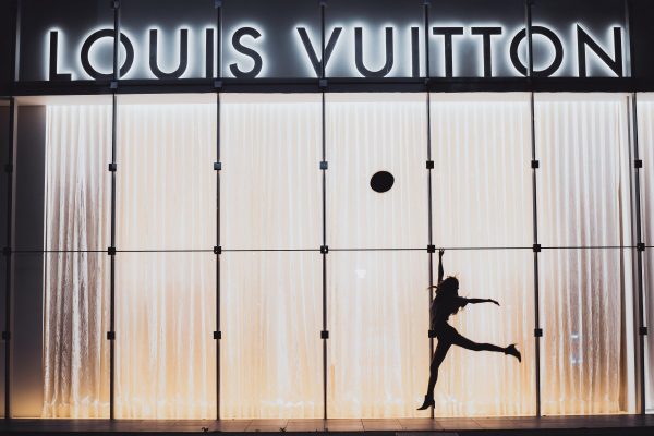 A woman jumping beside glass wall with louis vuitton signage