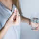 Woman holding half full glass and white medicine pill
