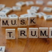 Scrabble tiles spelling musk and trump on wooden surface