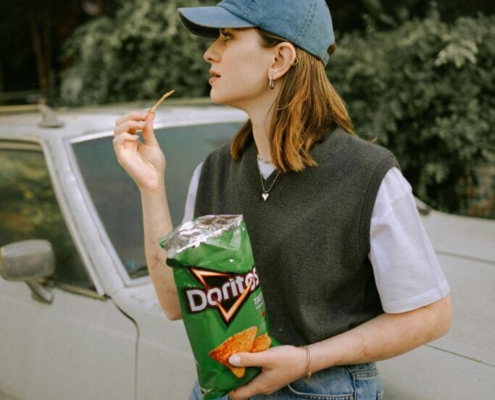 woman-in-cap-eating-doritos-by-car-stockpack-pexels.jpg Woman in cap eating doritos by car