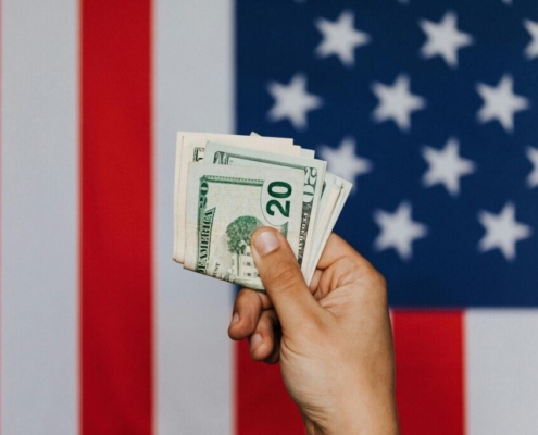Crop person showing pack of dollars against american flag