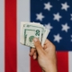 Crop person showing pack of dollars against american flag