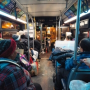 Inside a Jersey City bus at night, the interior is filled with daily commuters heading home after a long day. The bus, lit by the soft glow of overhead lights, captures the typical urban transit experience, with passengers seated.