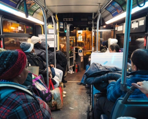 Inside a Jersey City bus at night, the interior is filled with daily commuters heading home after a long day. The bus, lit by the soft glow of overhead lights, captures the typical urban transit experience, with passengers seated.